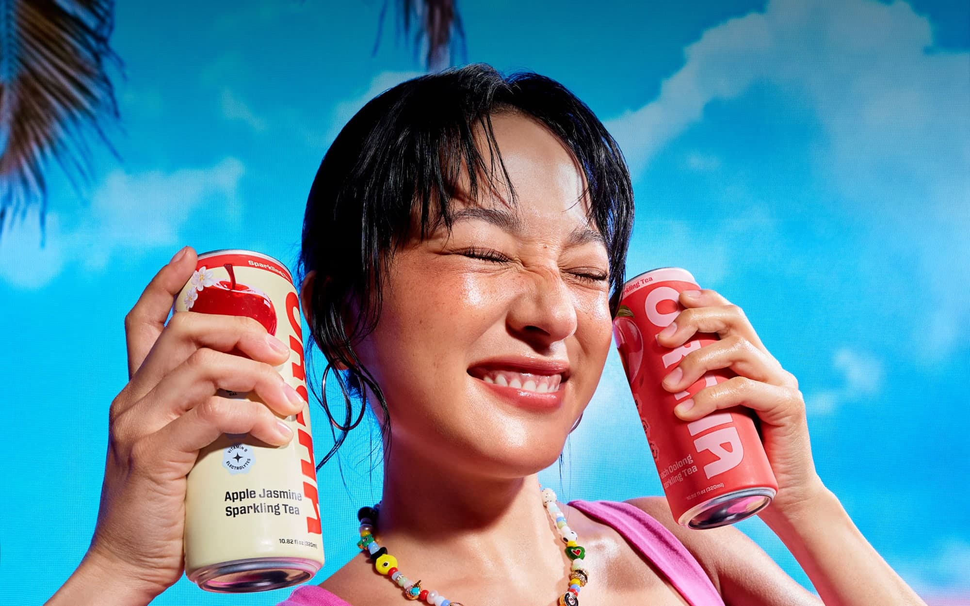 Two people holding Orcha sparkling tea cans under a blue sky.