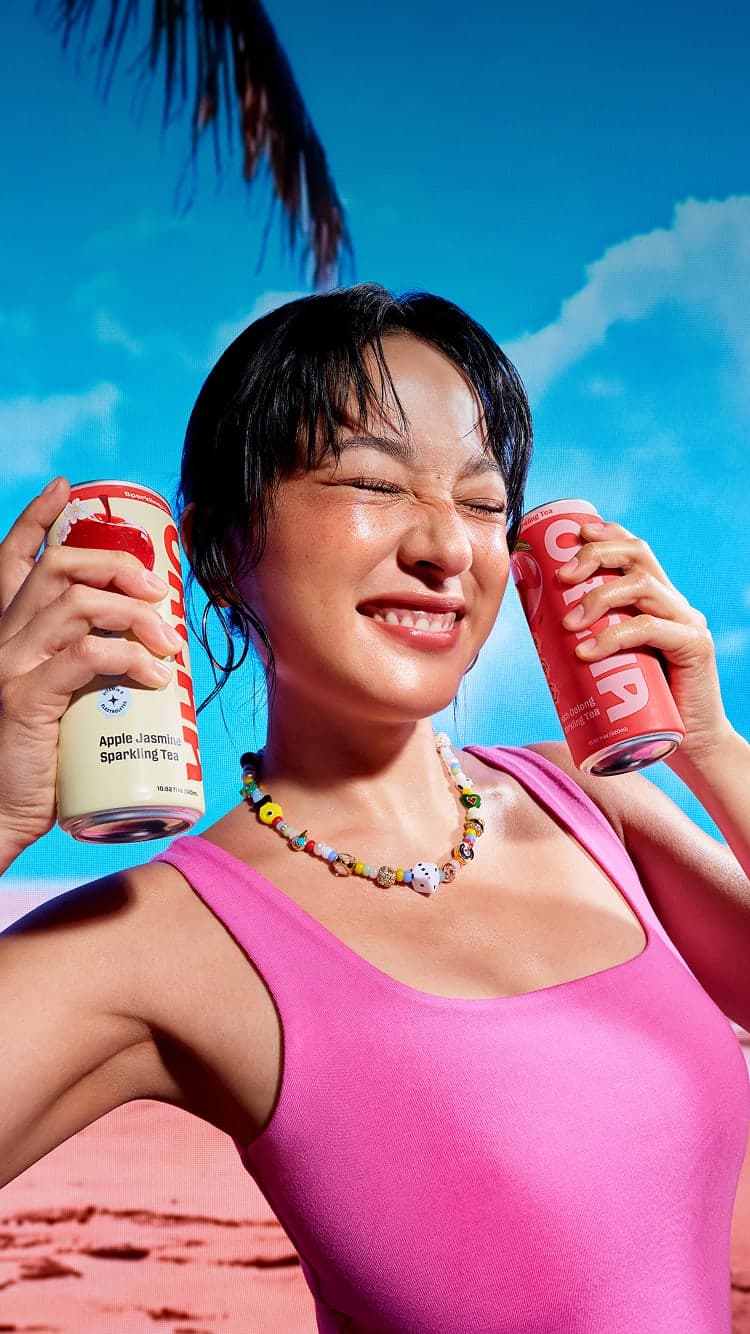 Two people holding Orcha sparkling tea cans under a blue sky.